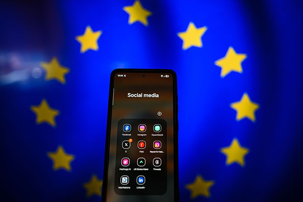 social media apps σε κινητό μπροστά από τη σημαία της ΕΕ